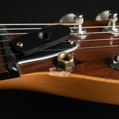 A close-up of a damaged electric guitar truss rod nut, showing signs of stripping from incorrect tools.